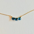 Gold necklace with three blue gemstones on a light gray background