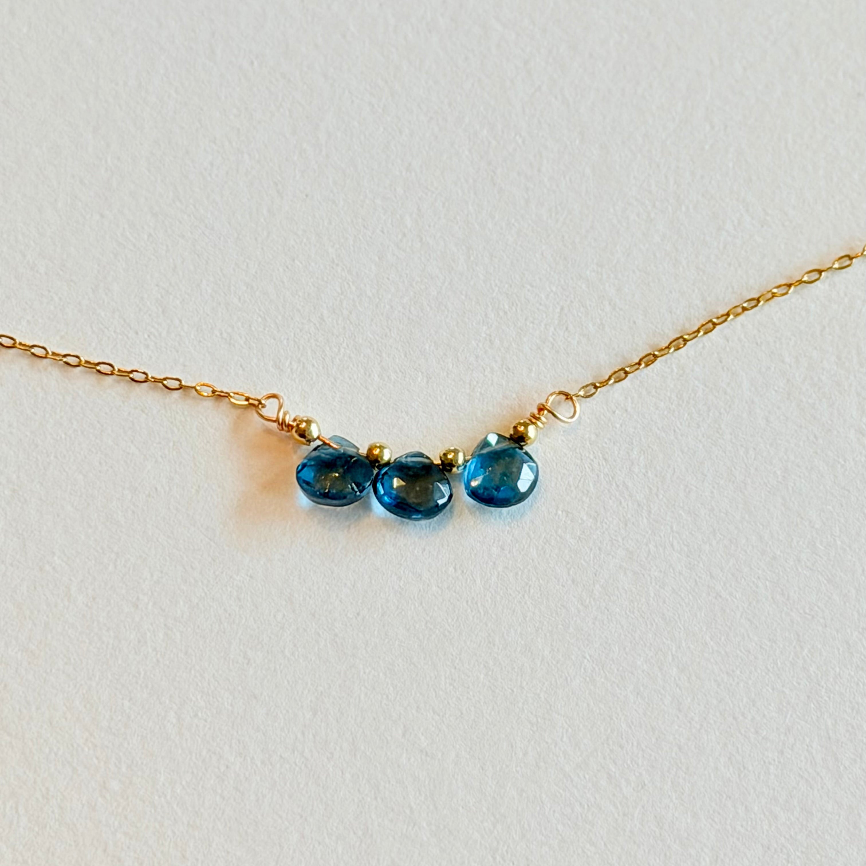 Gold necklace with three blue gemstones on a light gray background