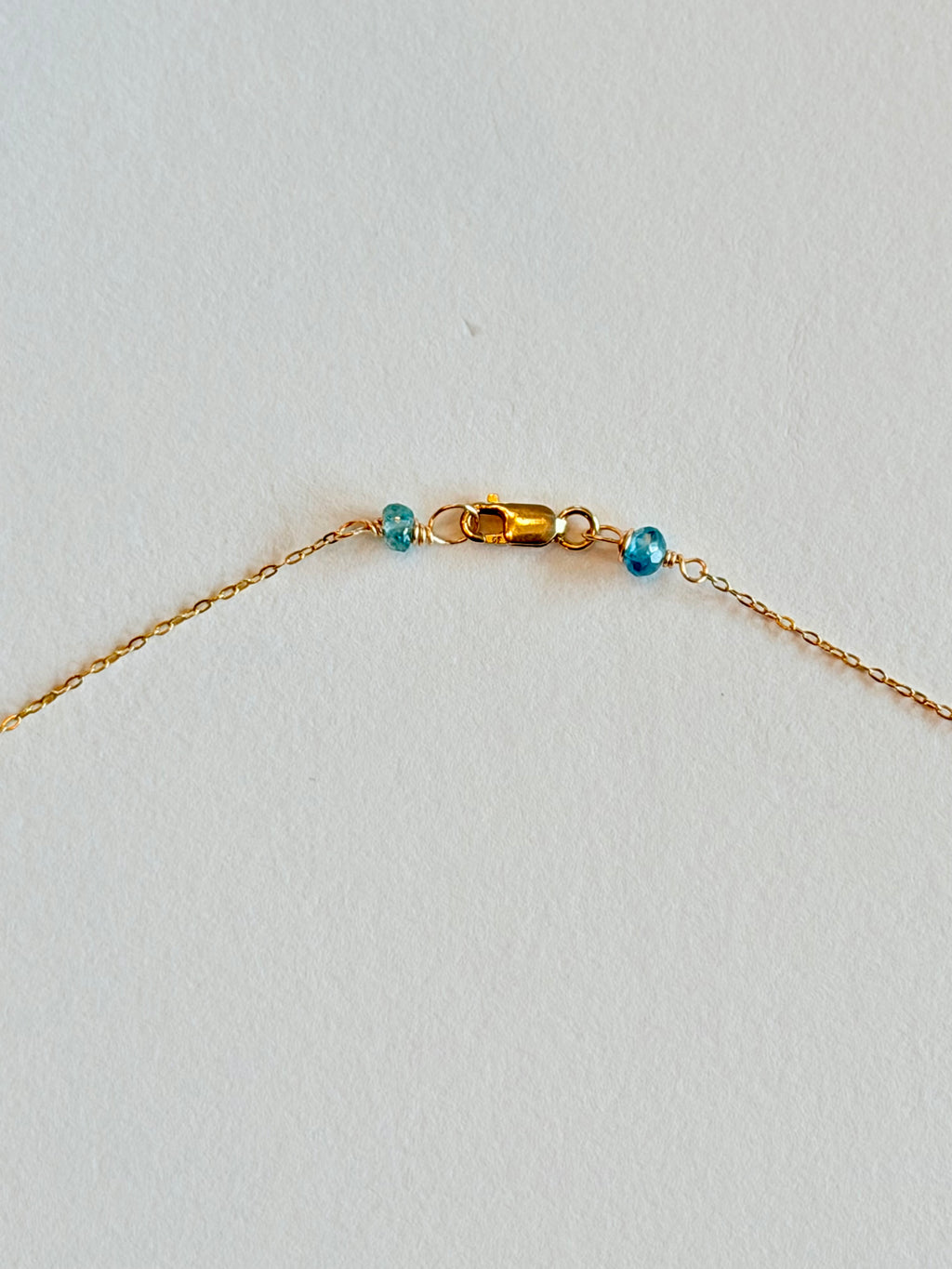 Gold necklace with blue beads on a light gray background