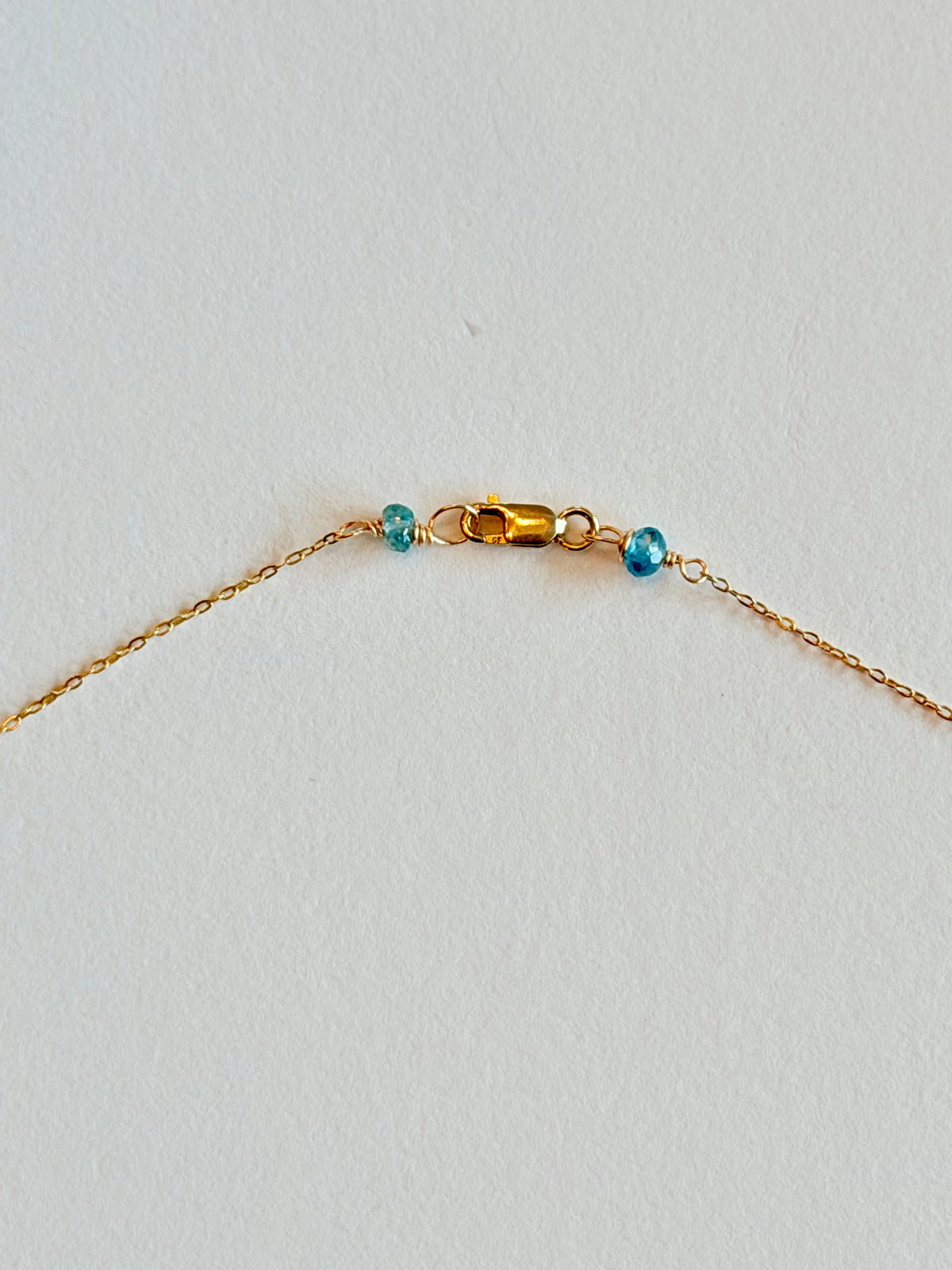 Gold necklace with blue beads on a light gray background