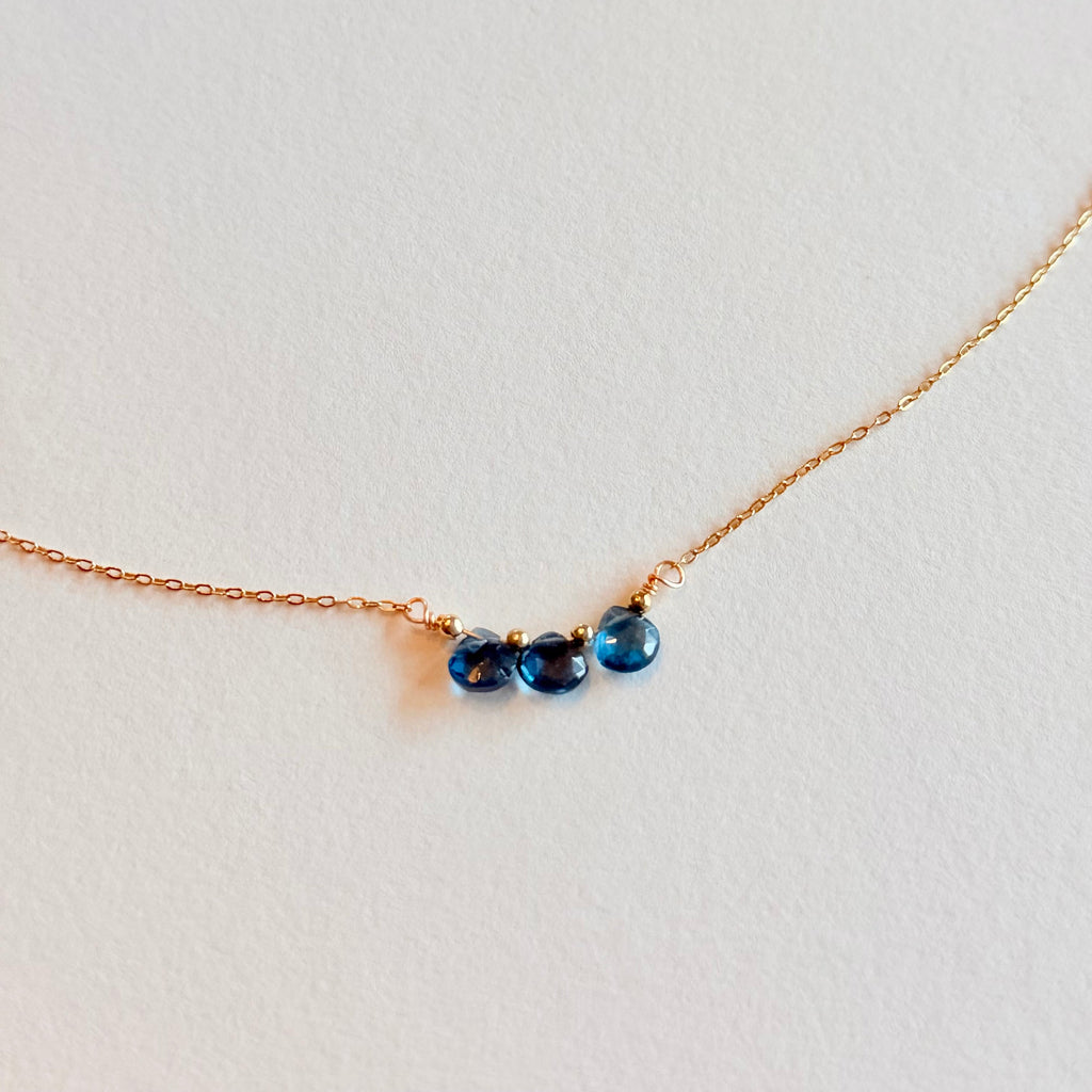 Gold necklace with three blue gemstones on a light gray background