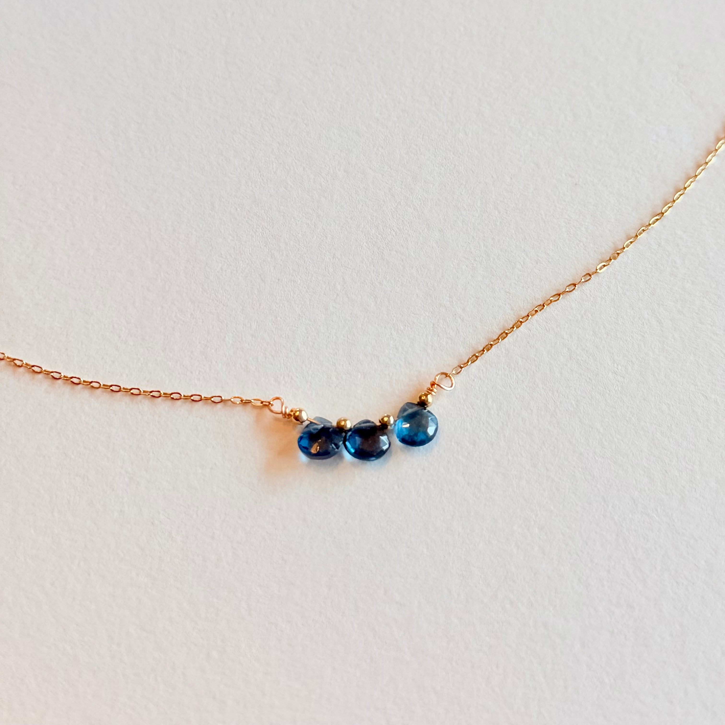 Gold necklace with three blue gemstones on a light gray background