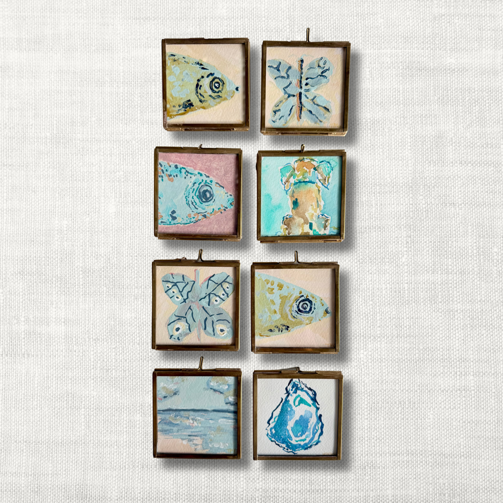 A set of eight small square framed art prints featuring various sea life illustrations like fish, a butterfly, an oyster, and a dog, arranged in a grid on a textured white linen background.