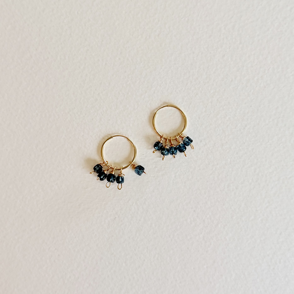 Gold hoop earrings with black beads on a light gray background