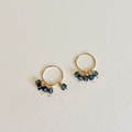 Gold hoop earrings with dark beads on a light gray background