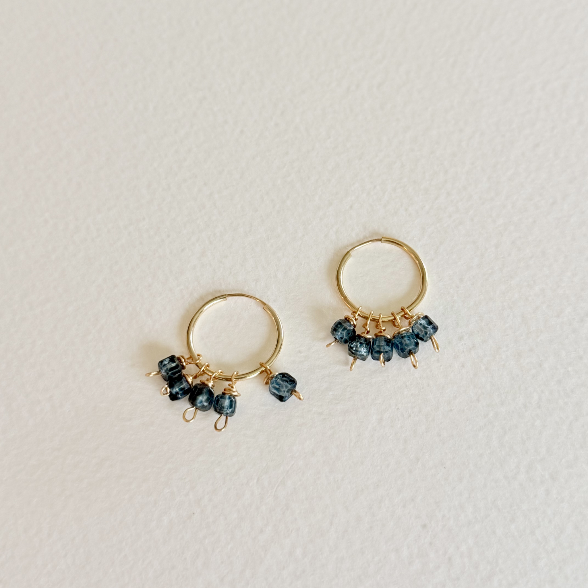 Gold hoop earrings with dark beads on a light gray background