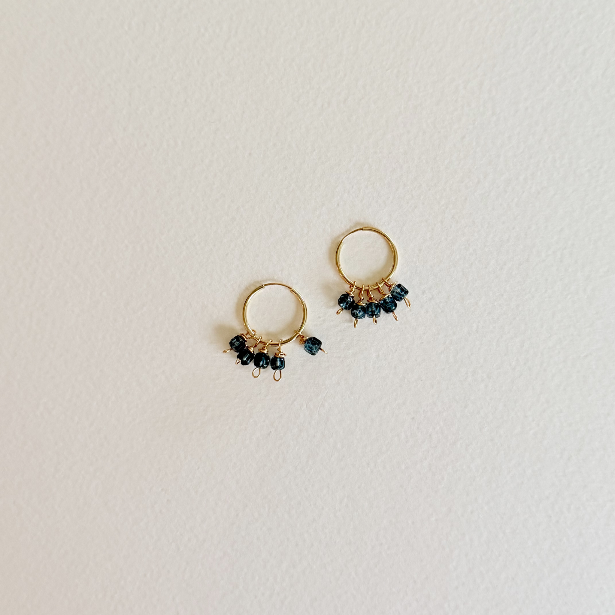 Pair of gold hoop earrings with small black beads on a light gray background