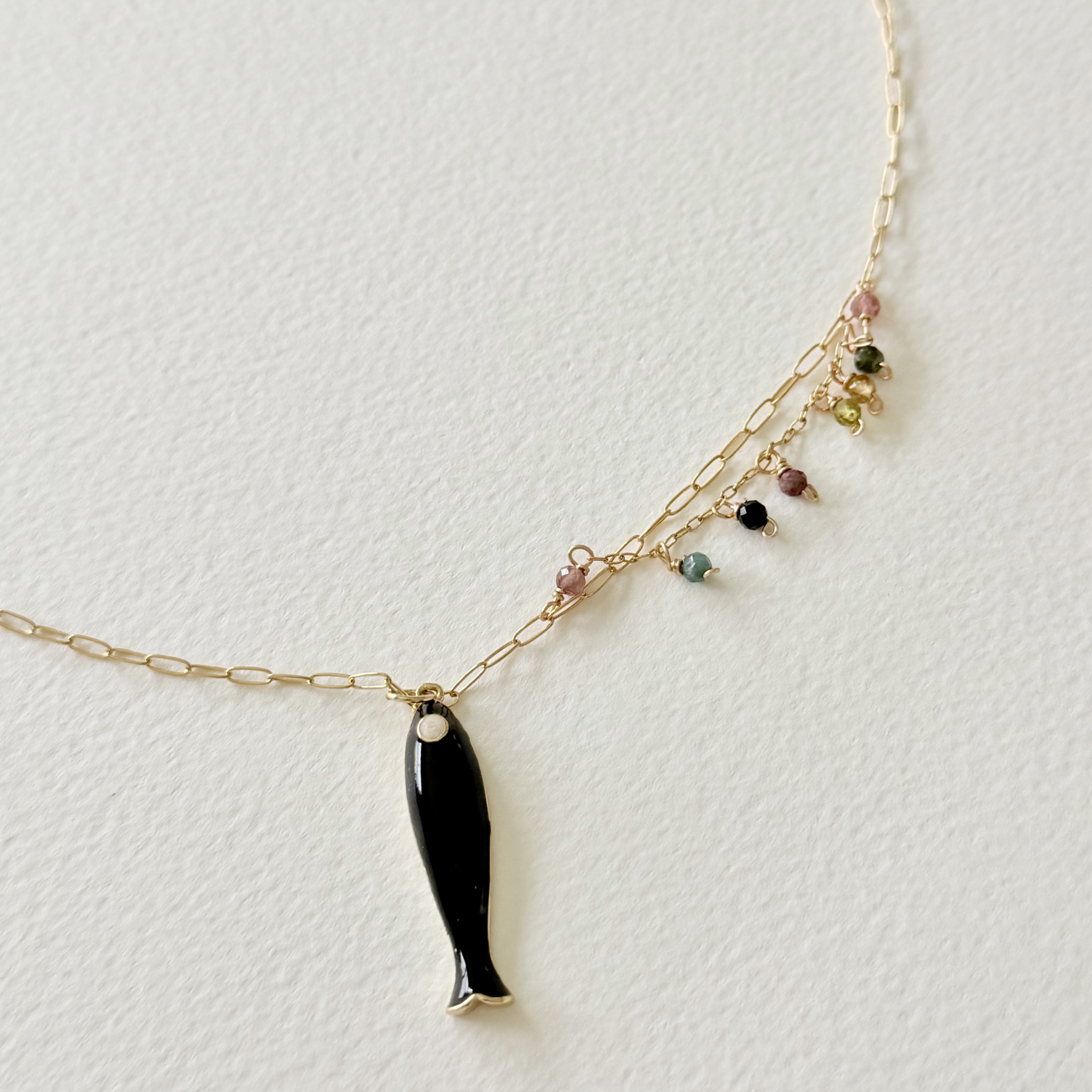 Necklace with a black fish pendant and multicolored beads on a light gray background