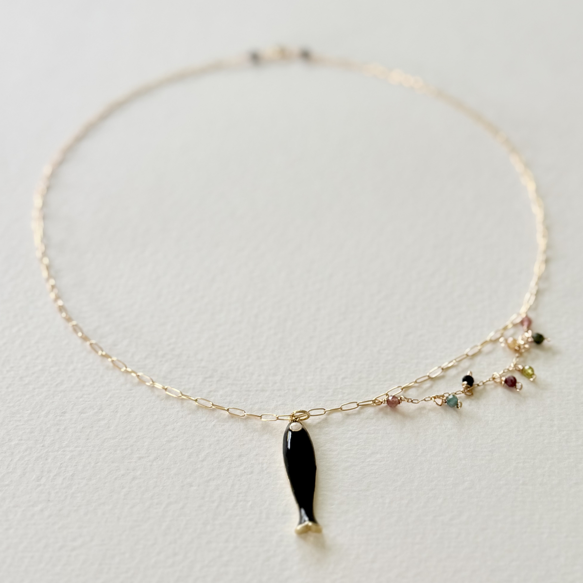 Delicate gold necklace with a black fish charm on a light gray background