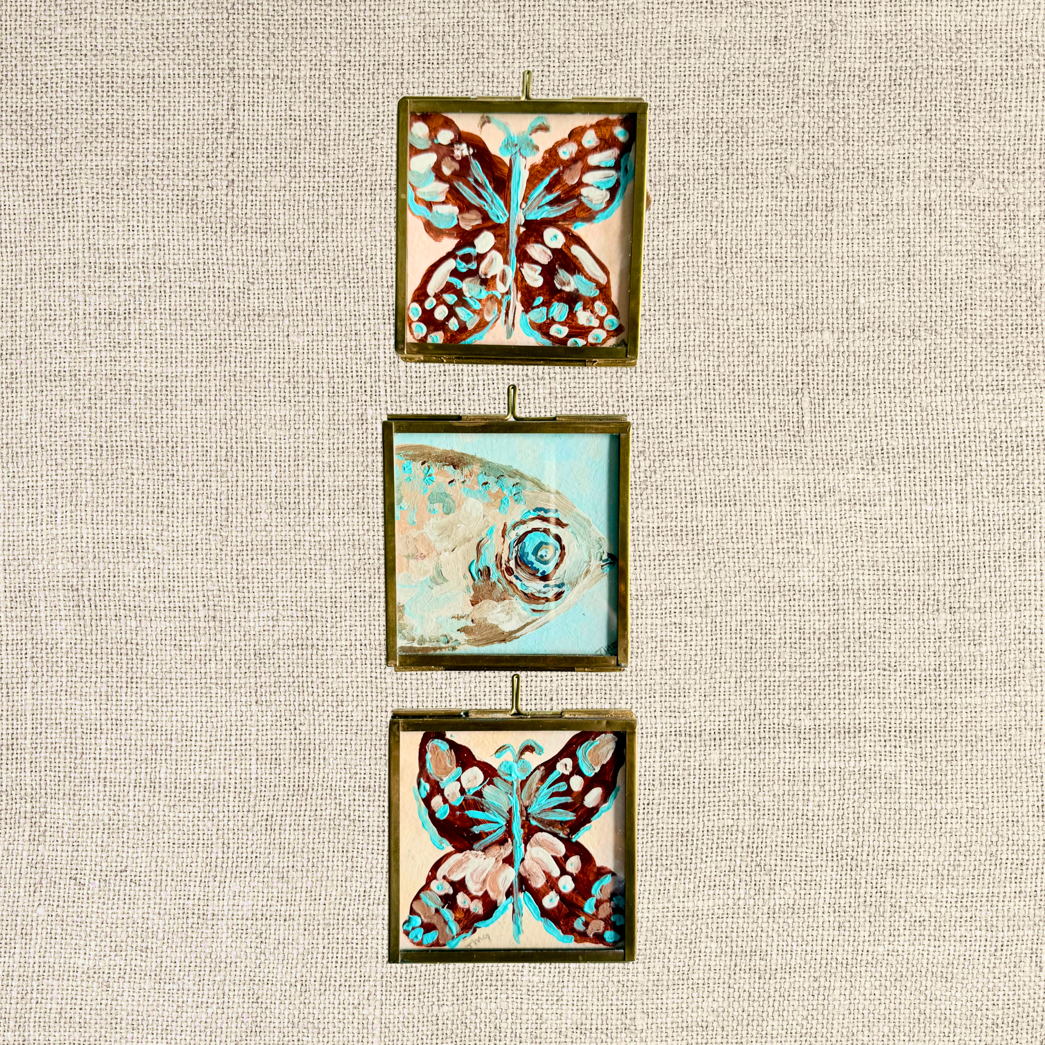 Three mini original coastal paintings in vintage-inspired brass frames featuring two butterflies and a fish in turquoise, rust and neutral tones.