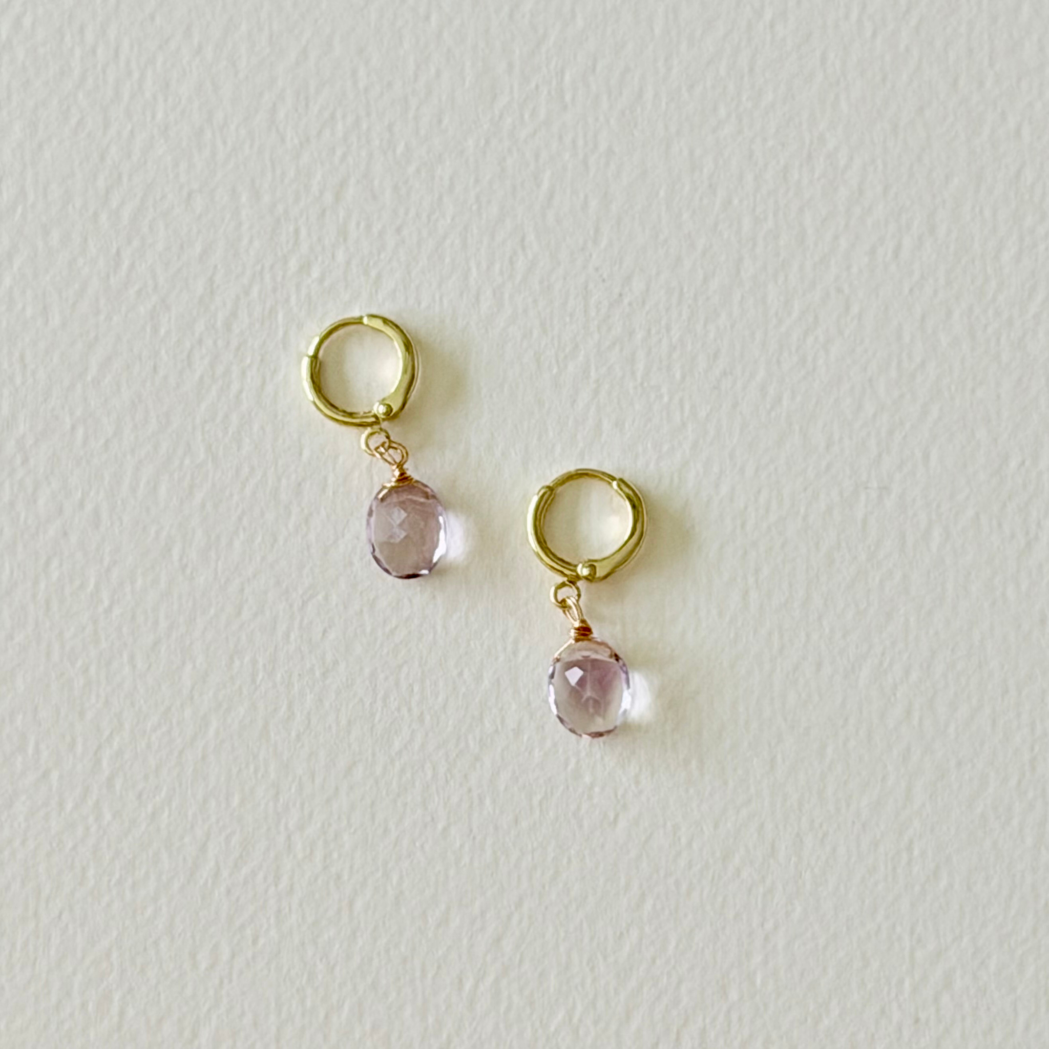 Gold hoop earrings with pink gemstones on a light gray background