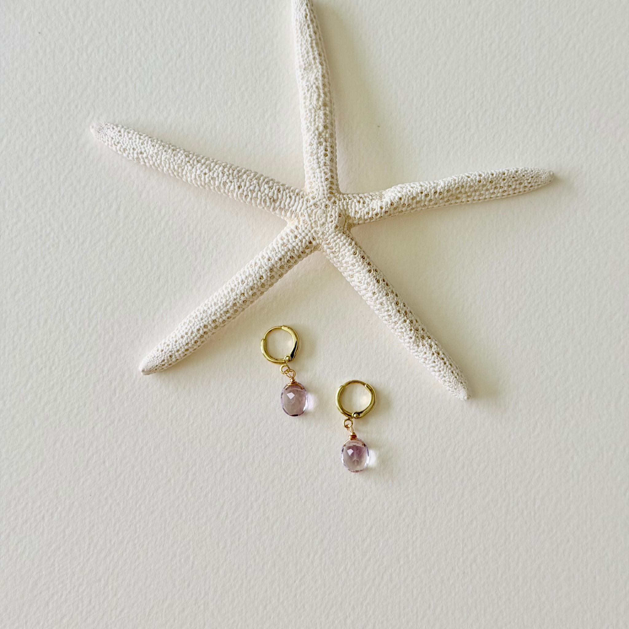Gold earrings with pink gemstones on a textured white surface with a starfish.