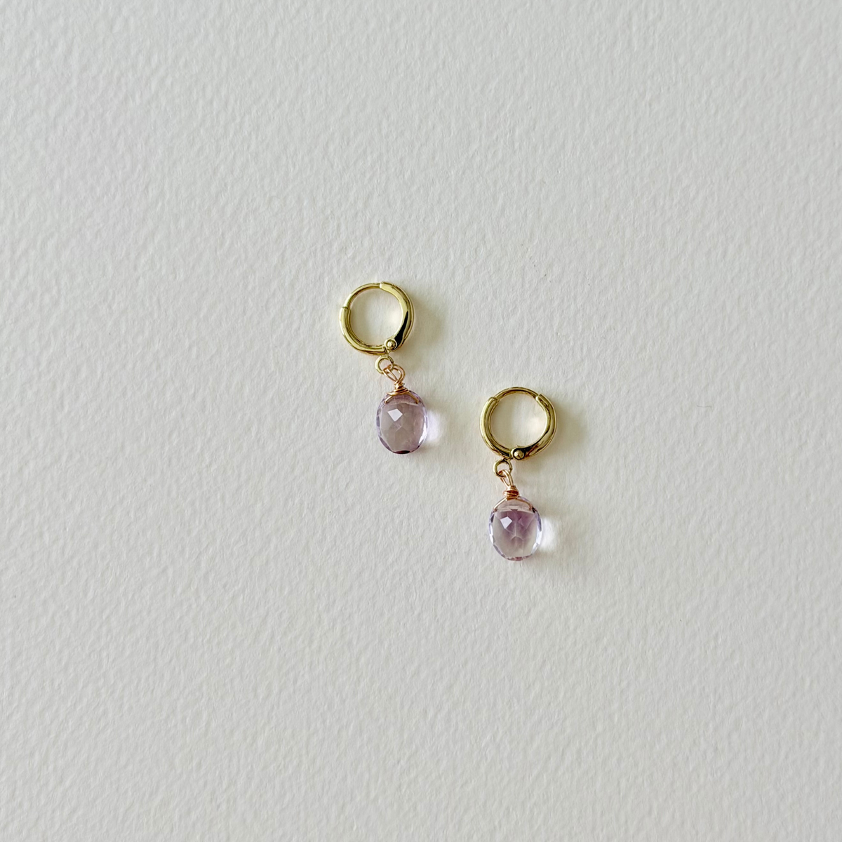Pair of gold earrings with purple gemstones on a light gray background