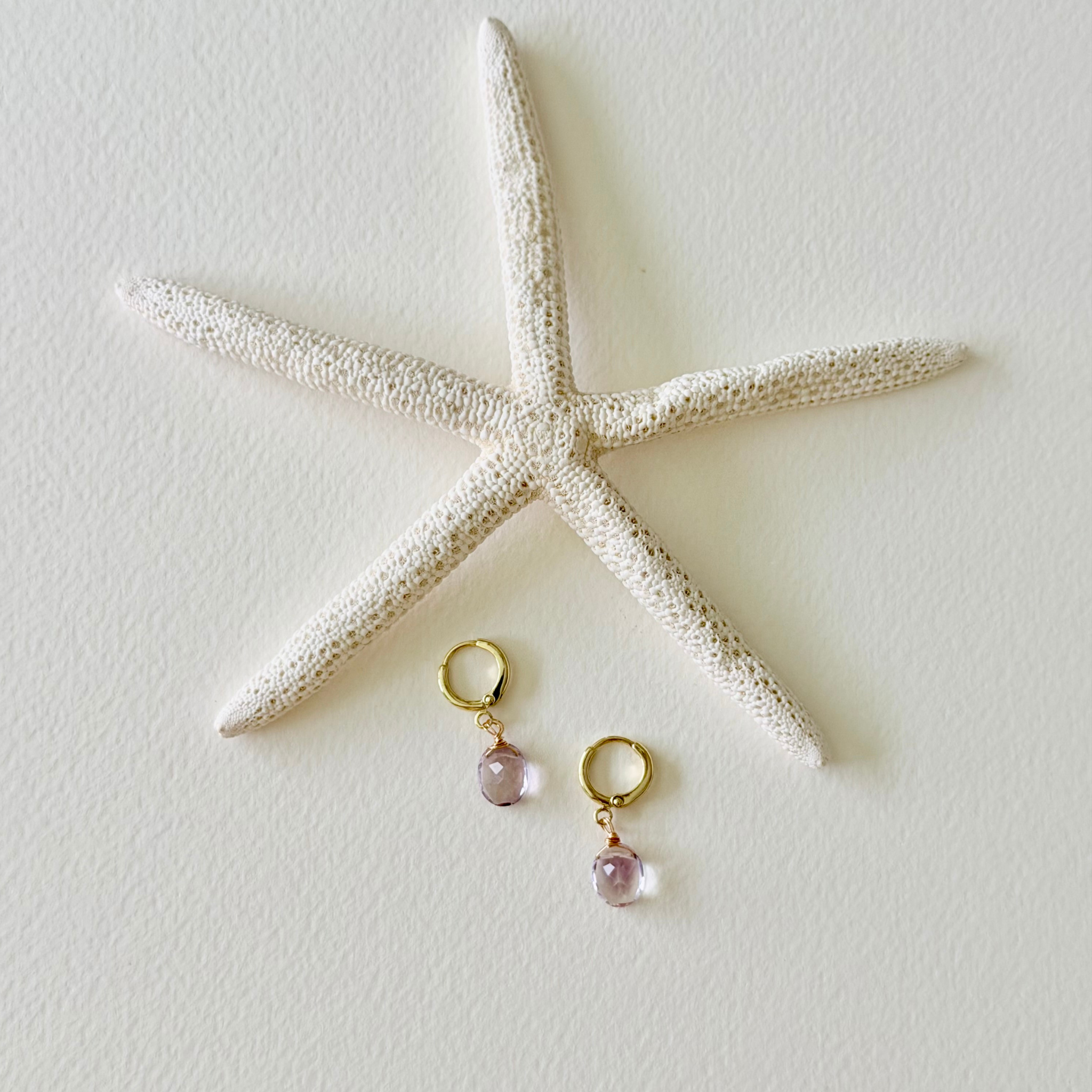 Pair of earrings with pink beads on gold hooks next to a starfish on a light background