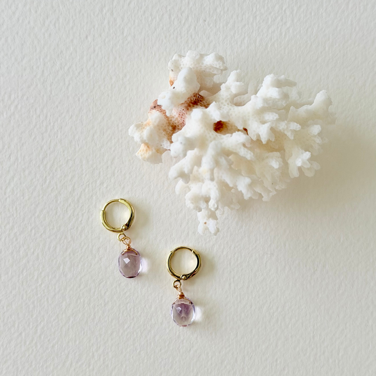 Gold earrings with pink gemstones on a white background with coral.
