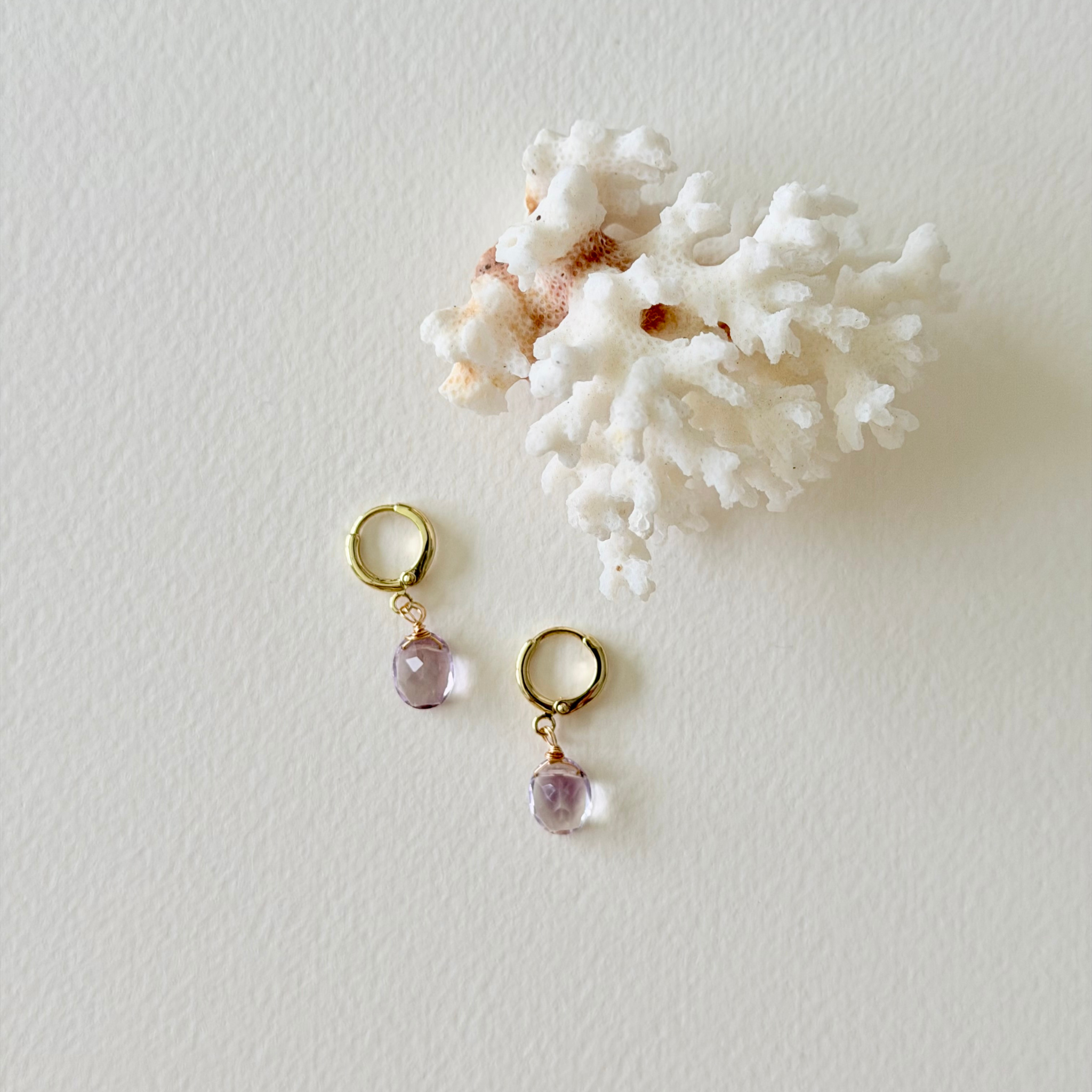 Pair of gold earrings with pink gemstones on a white background with coral.