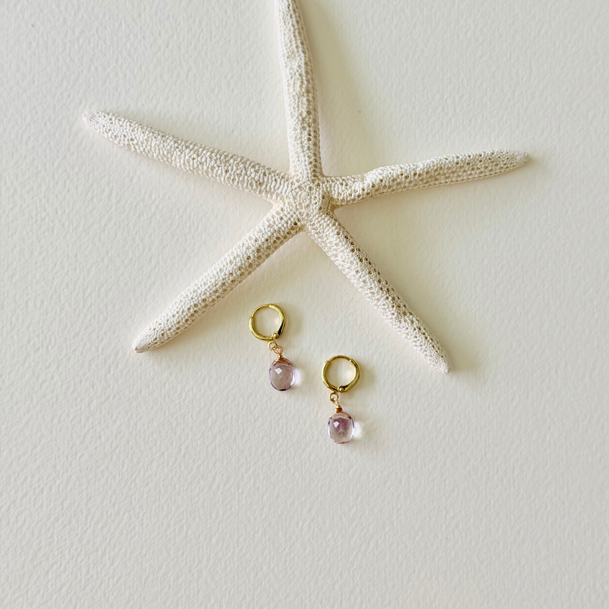 Pair of gold earrings with pink beads on a white surface with a starfish.