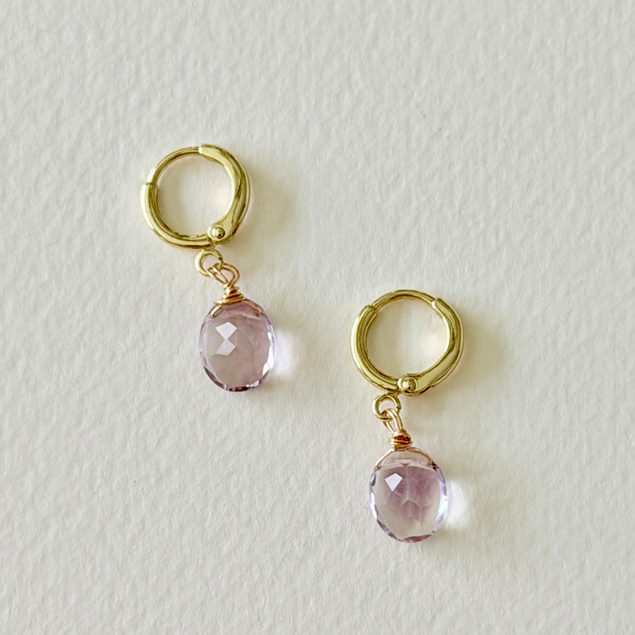 Gold hoop earrings with pink gemstones on a light gray background