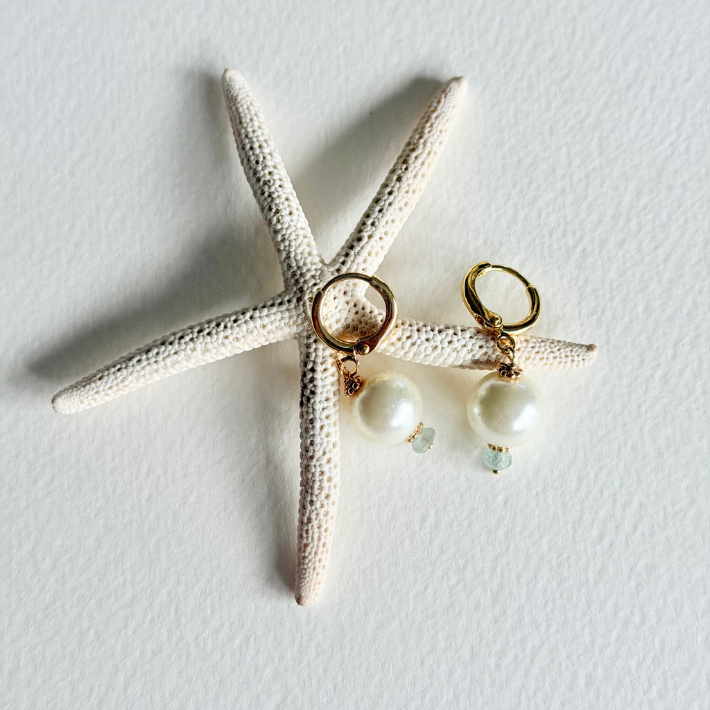 Pair of earrings with pearl-like beads on a starfish-shaped object against a light gray background