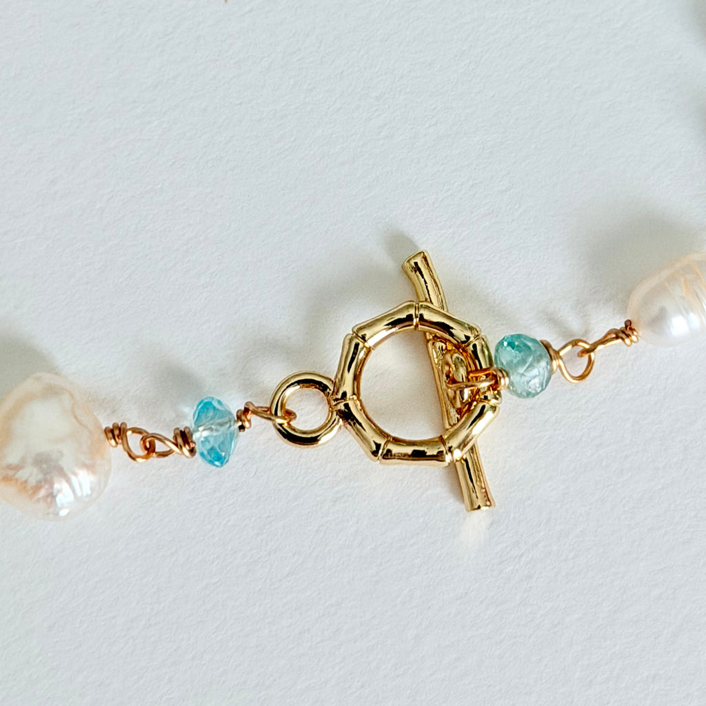 Close-up of a gold clasp with pearls and blue beads on a light background