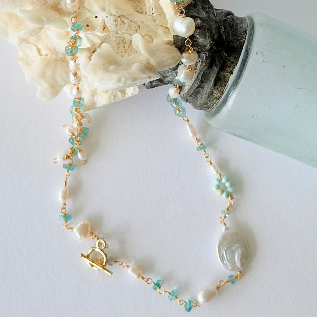 Necklace with pearls and turquoise beads on a white surface with coral and a bottle.