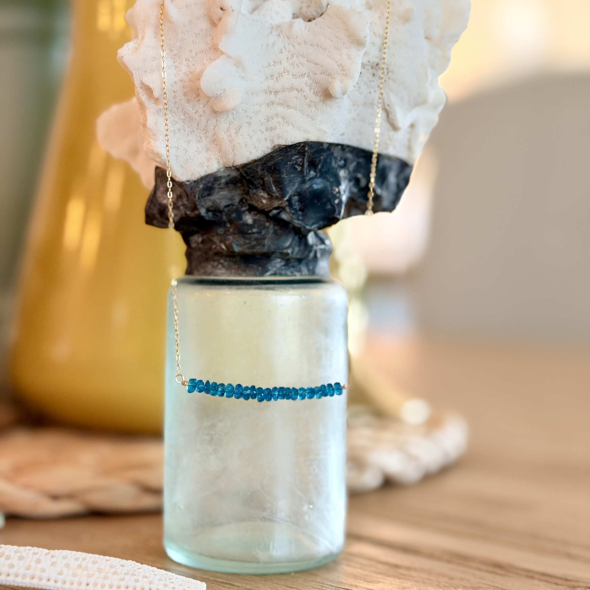 Blue beaded necklace on a glass stand with coral and shell decorations.