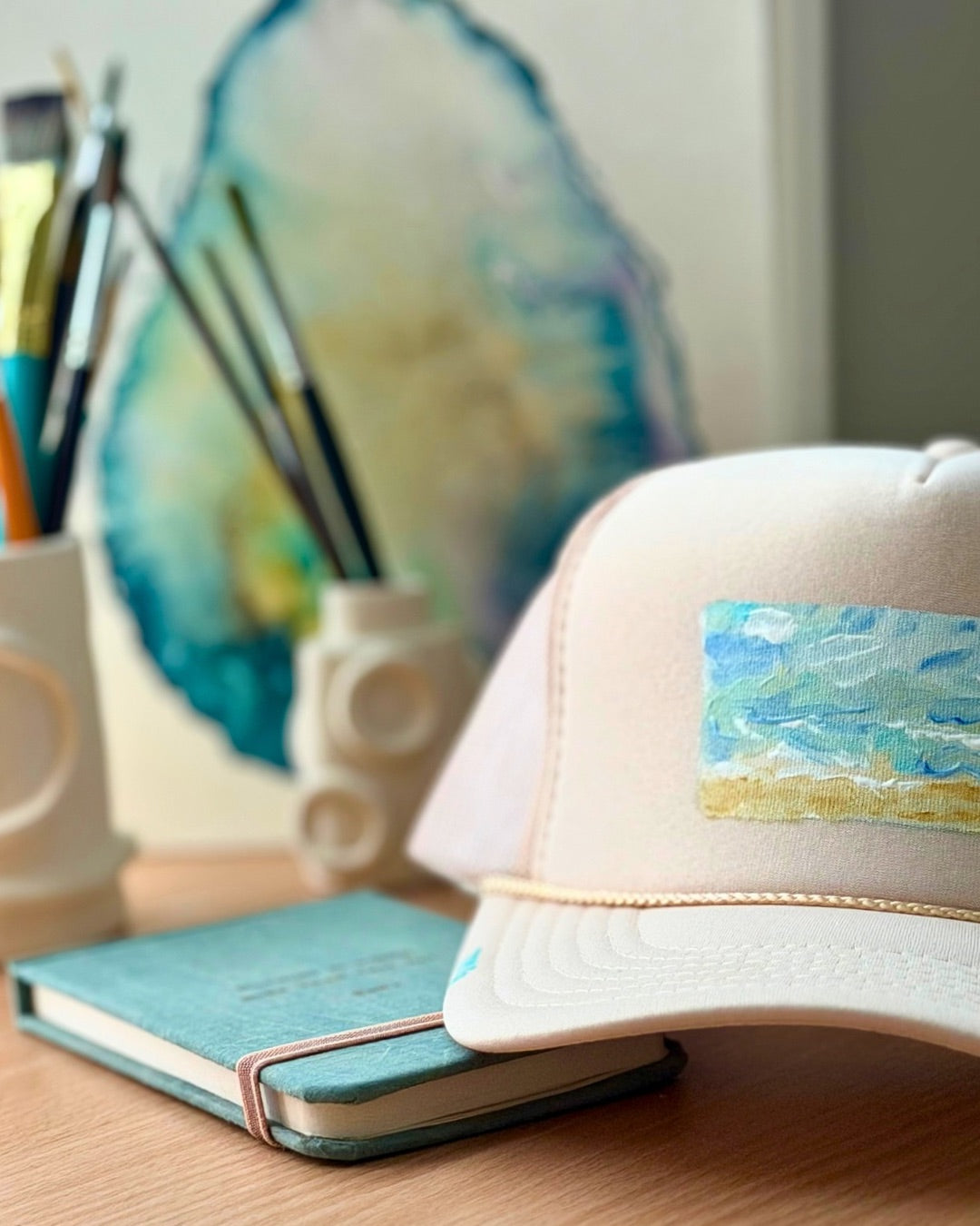 Cream hand-painted trucker hat featuring original textured ocean artwork in turquoise, blue and sandy gold by Marie & Oakley.