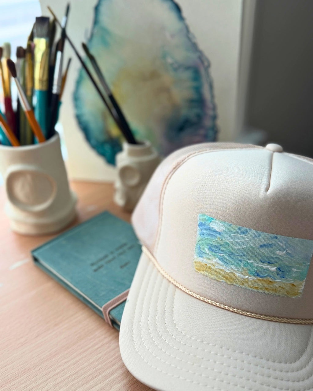 Cream hand-painted trucker hat featuring original textured ocean artwork in turquoise, blue and sandy gold by Marie & Oakley.