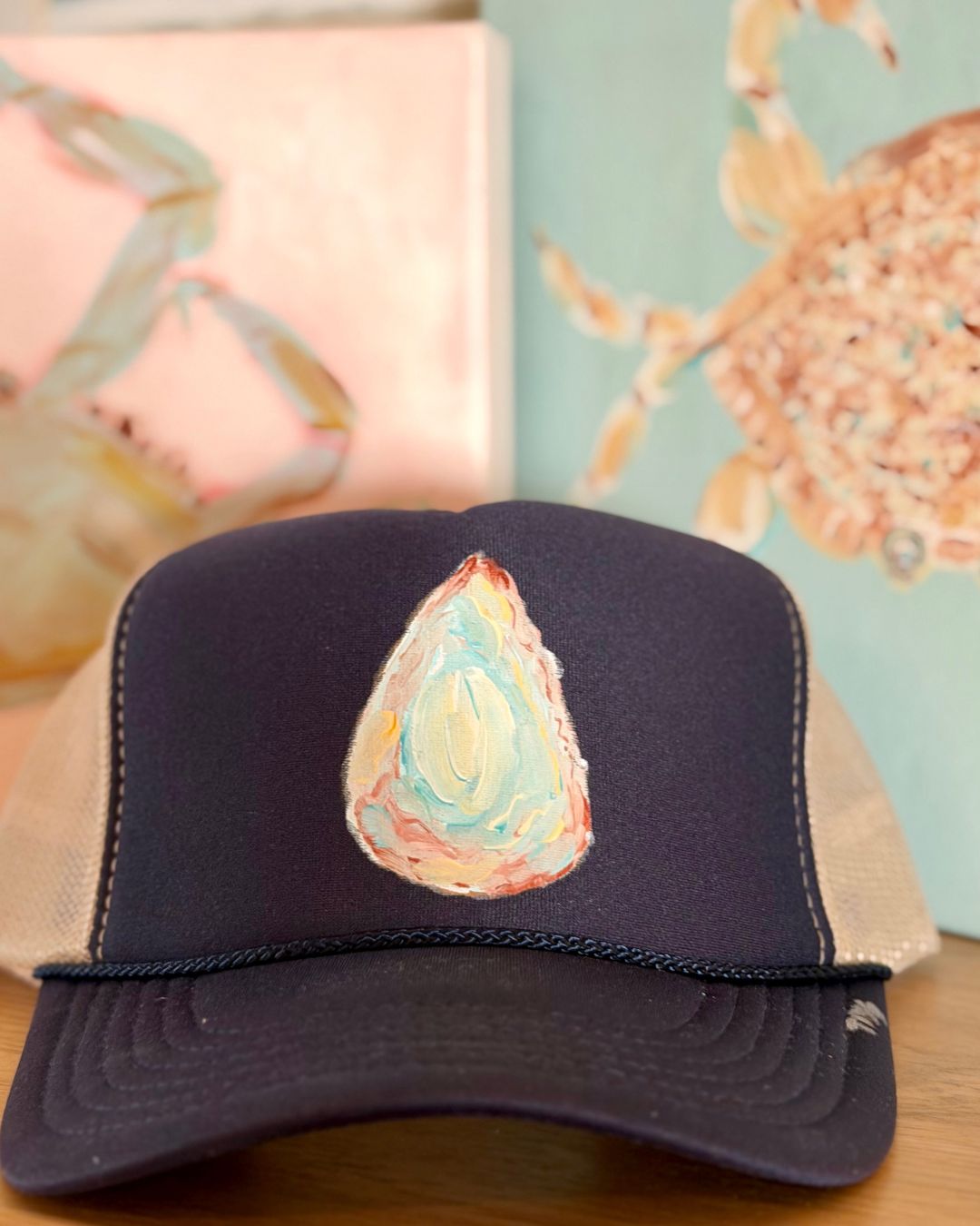 navy blue  trucker hat featuring a colorful hand-painted oyster shell inspired by coastal living, original wearable art by Marie & Oakley.