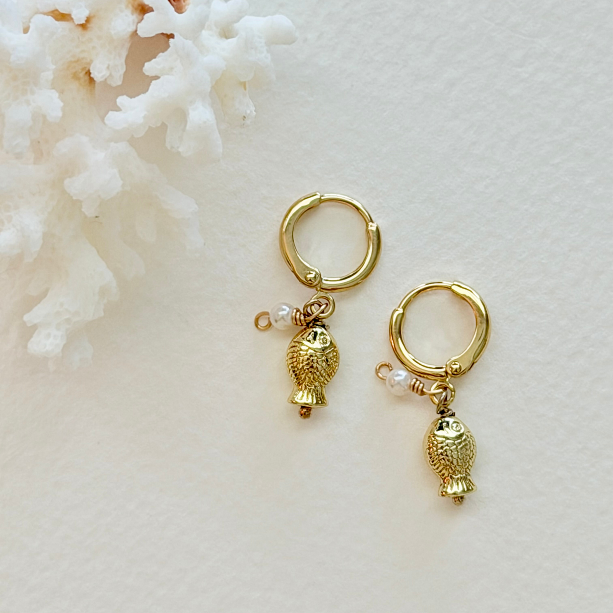 Gold hoop earrings with fish charms on a white background