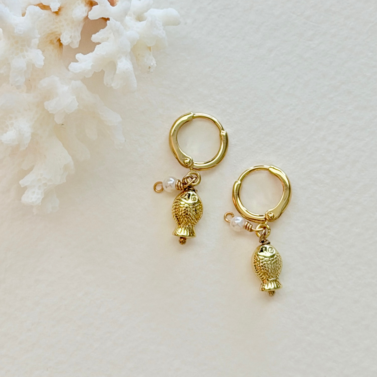 Gold hoop earrings with fish charms on a white background