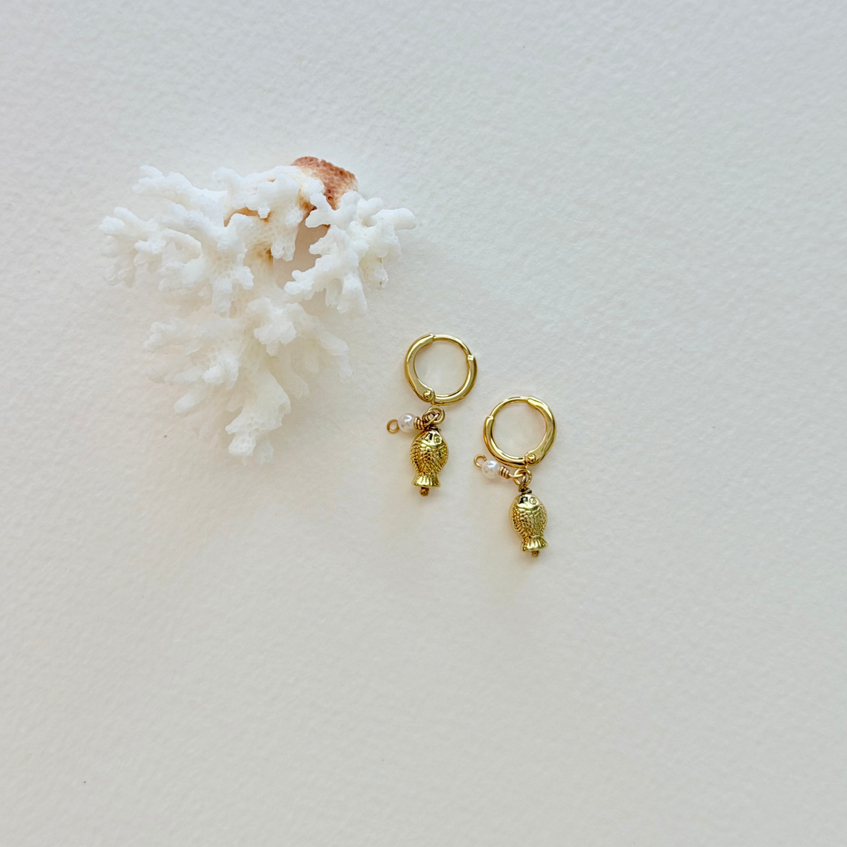 Gold earrings on a light background with coral