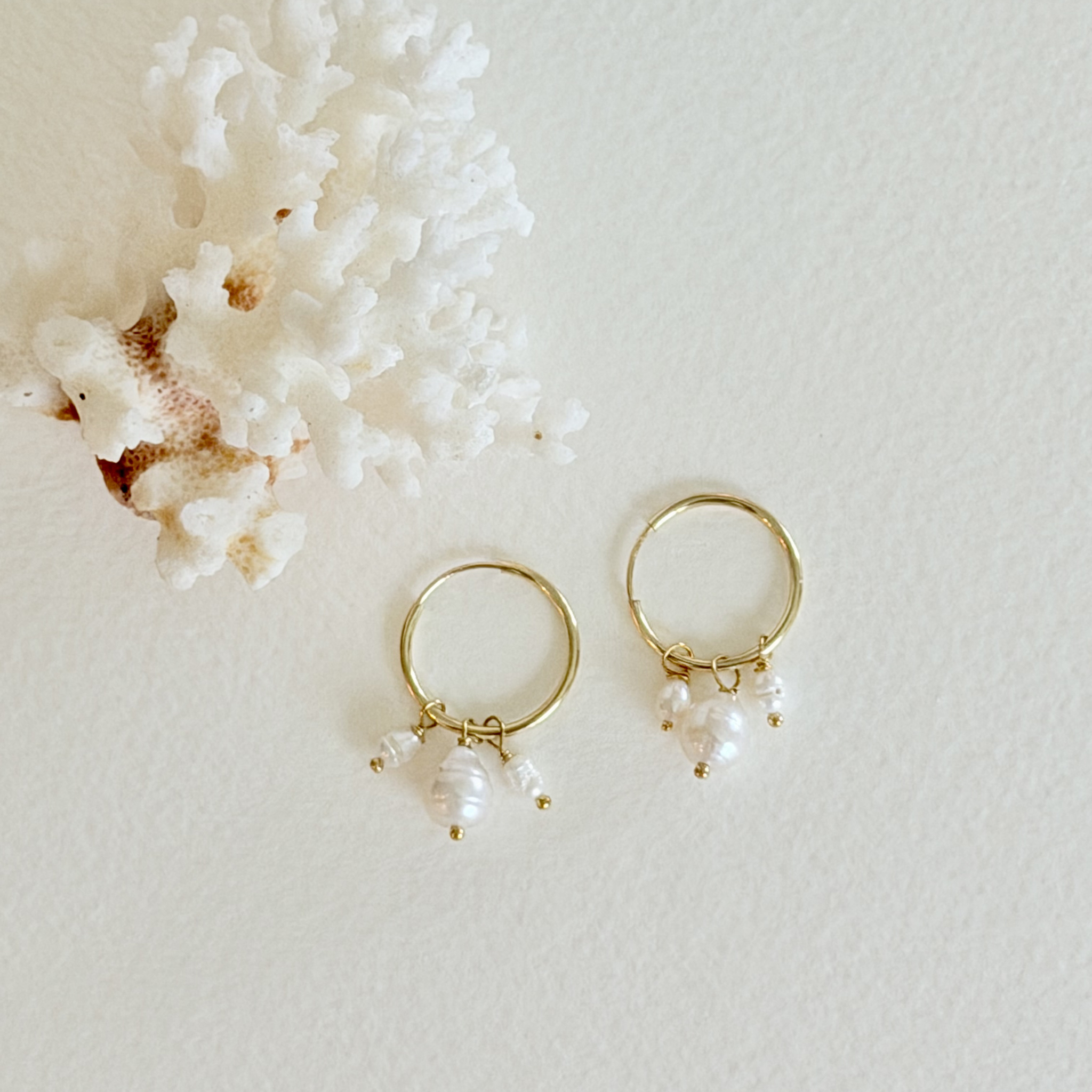 Gold hoop earrings with pearl-like beads on a textured white surface