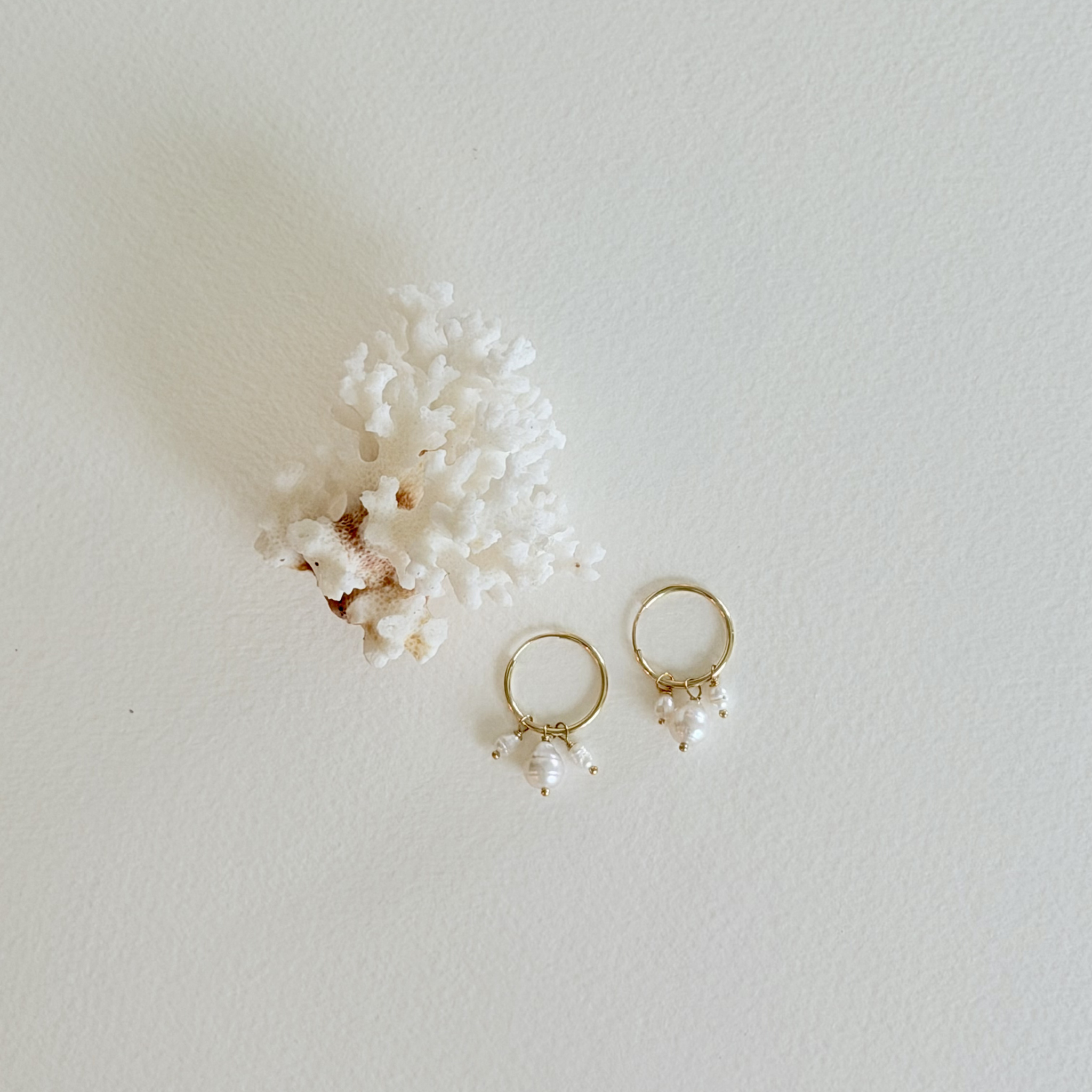 Gold hoop earrings with pearl drops on a light gray background