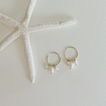 Gold hoop earrings with pearl drops next to a starfish on a light background
