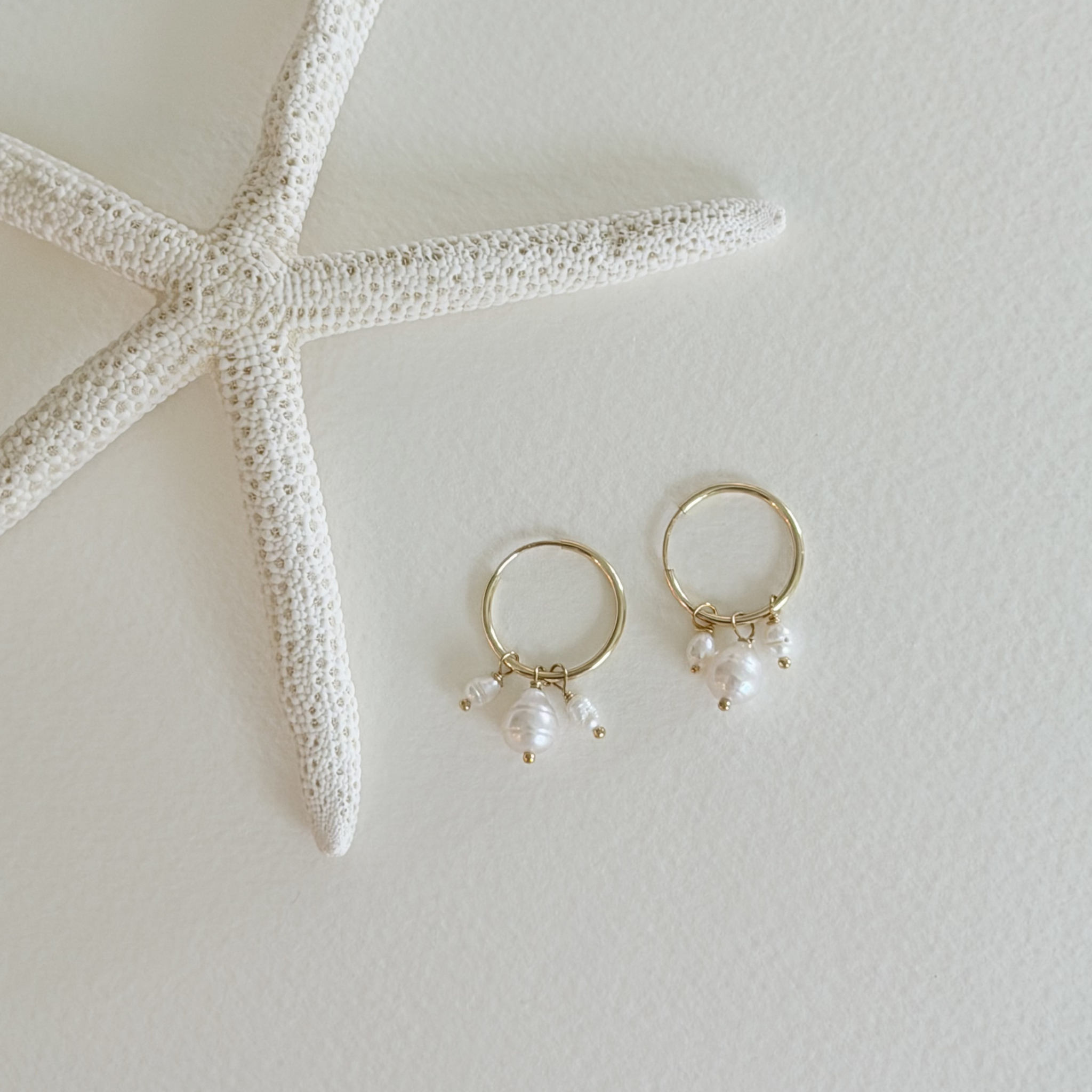 Gold hoop earrings with pearl drops next to a starfish on a light background