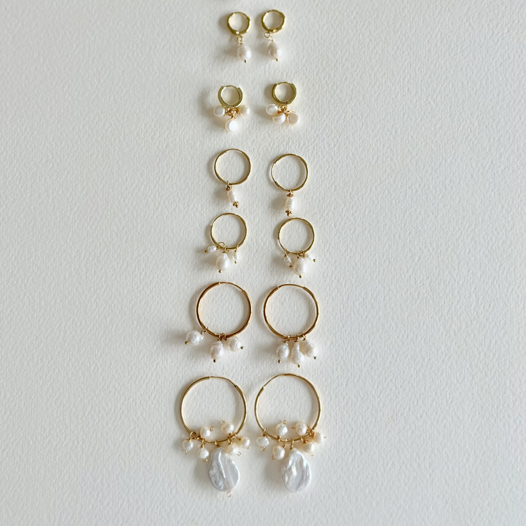 Collection of gold hoop earrings with pearl drops on a light gray background