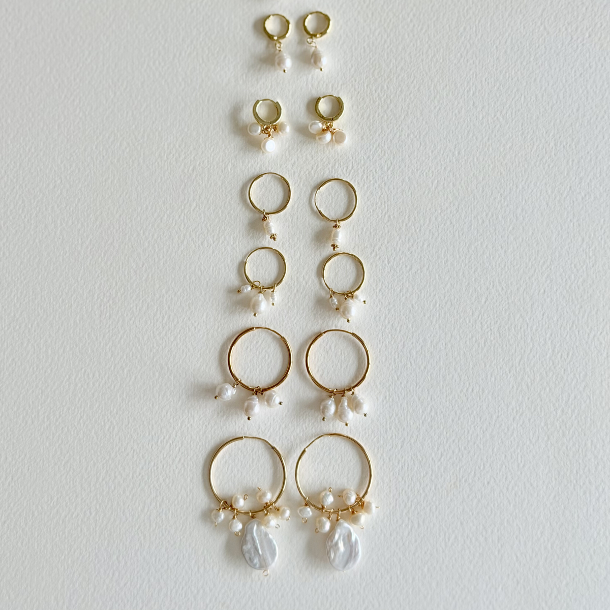 Collection of gold hoop earrings with pearl drops on a light gray background