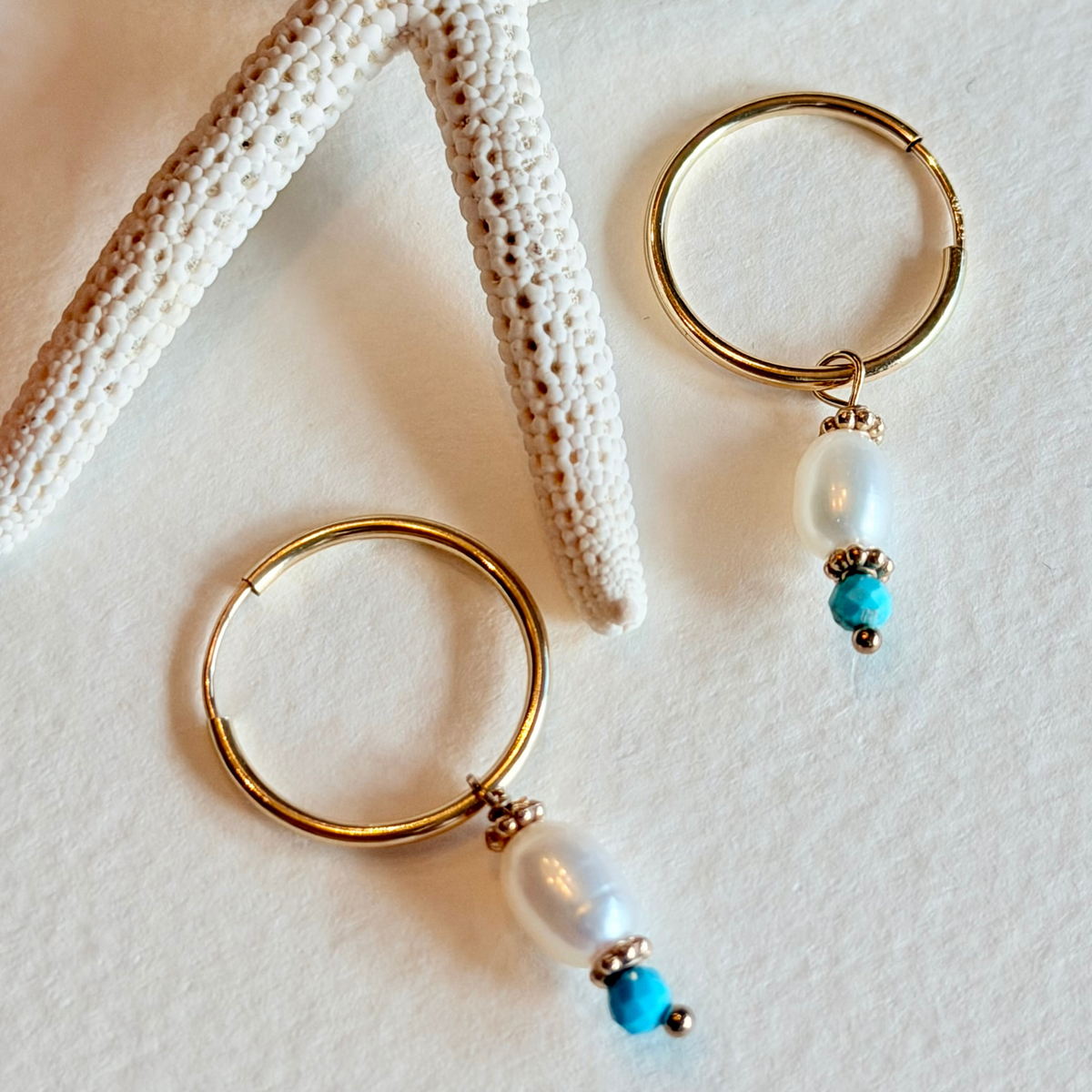 Gold hoop earrings with pearl and turquoise beads on a textured white surface