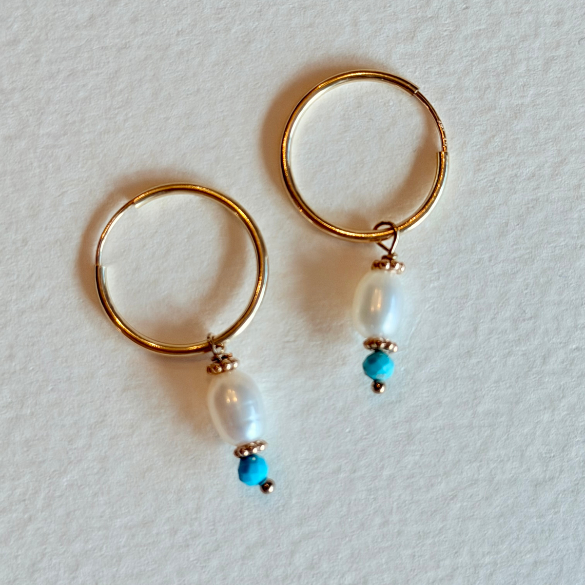 Gold hoop earrings with pearls and turquoise beads on a light gray background