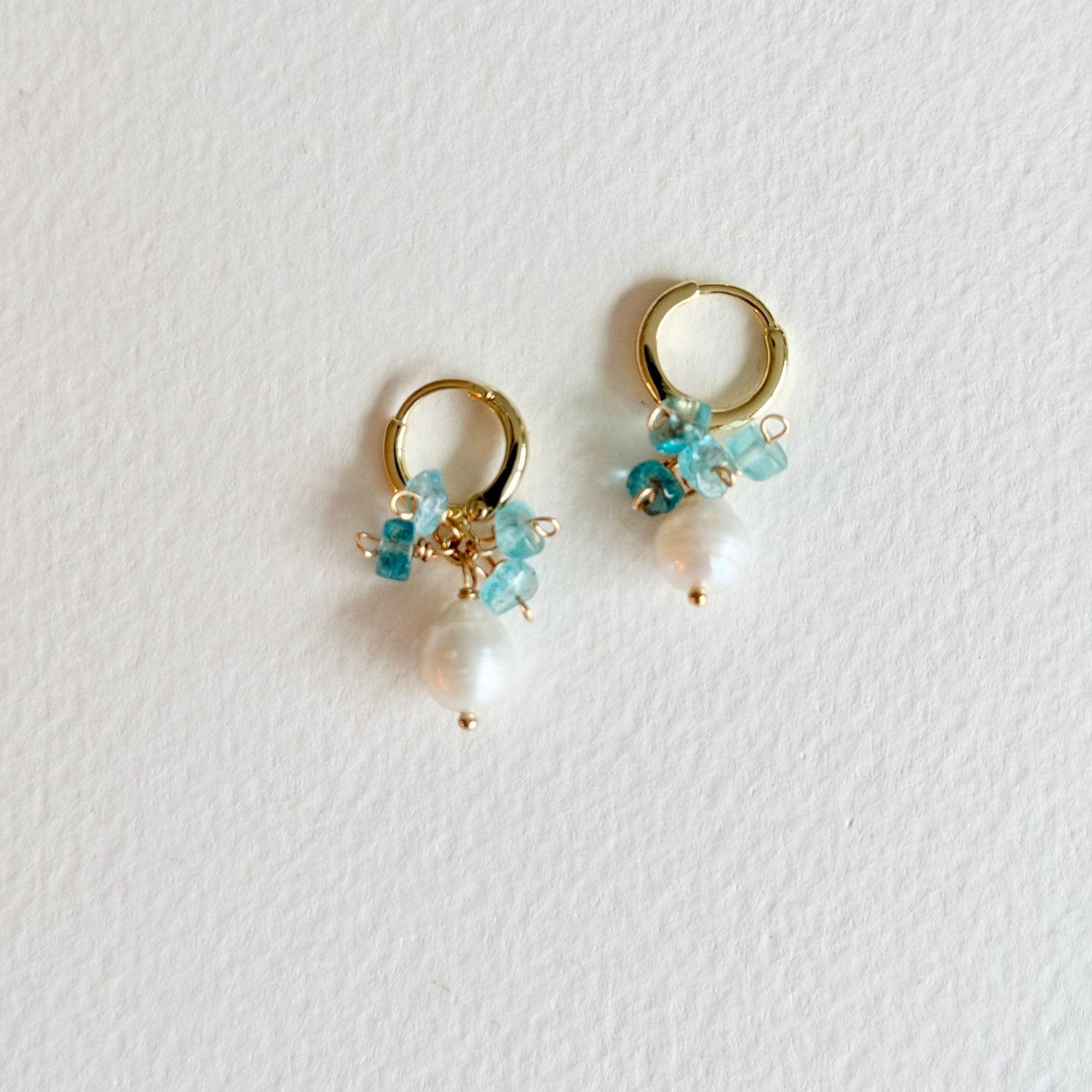 Pair of gold hoop earrings with turquoise beads and pearls on a light gray background