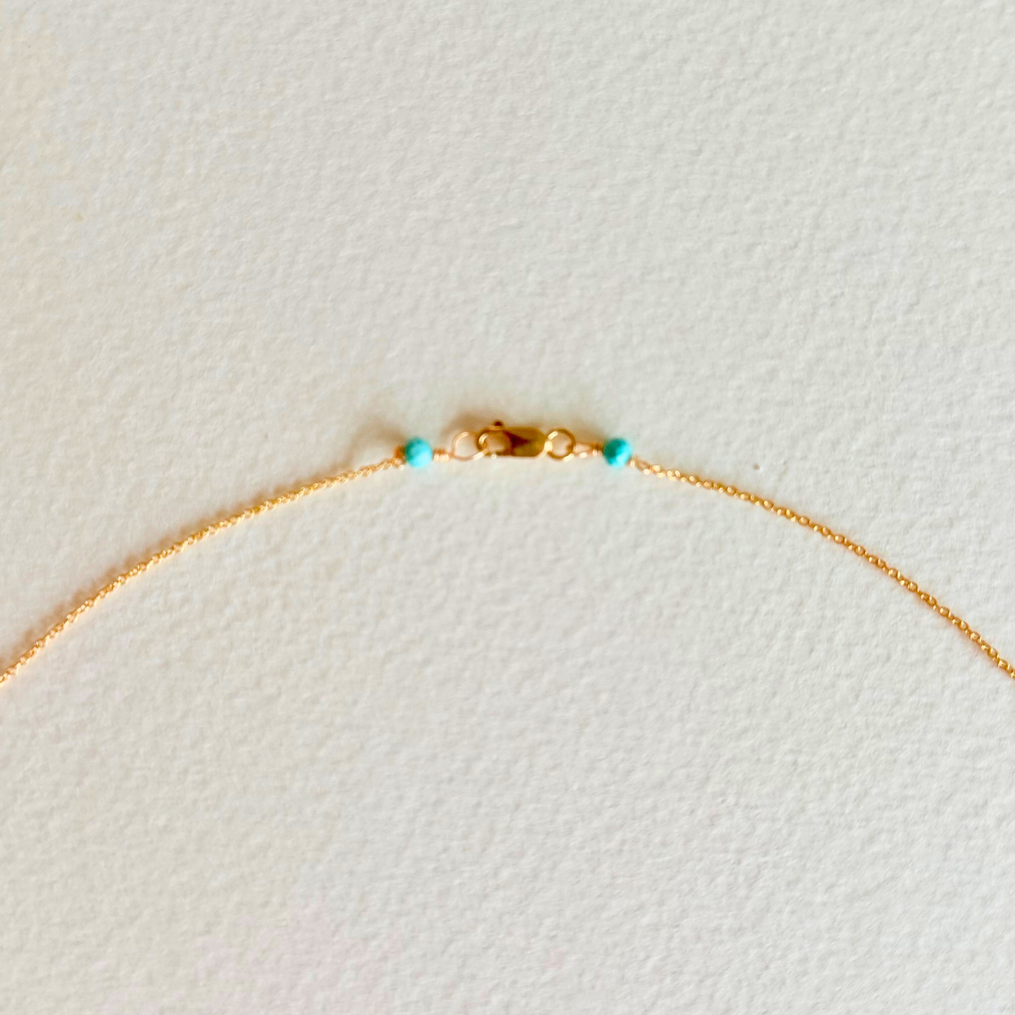 Gold necklace with turquoise beads on a light beige background