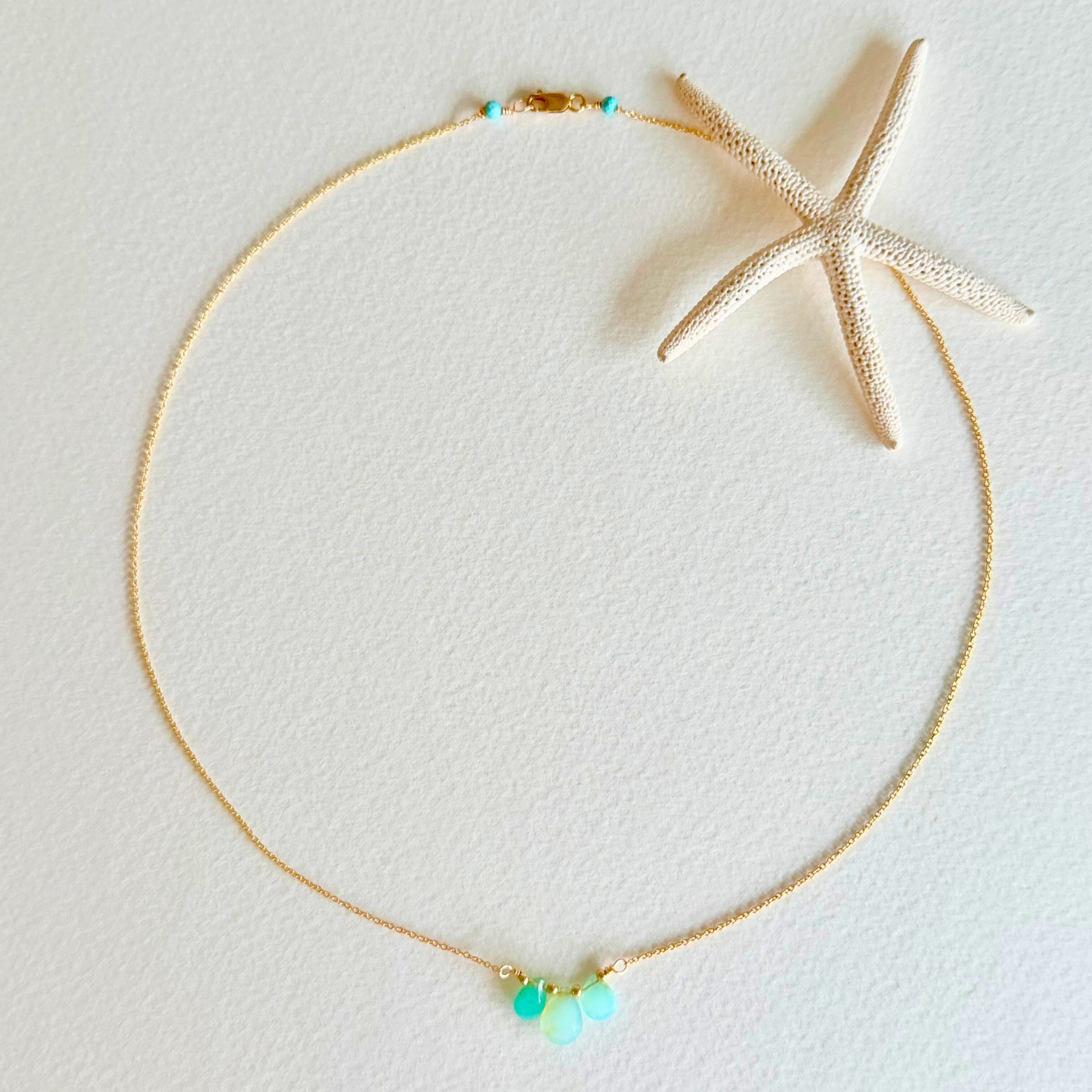Gold necklace with green beads on a light gray background