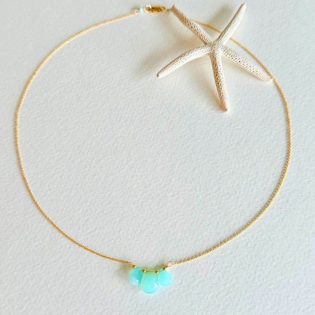 Gold necklace with turquoise beads on a light gray background