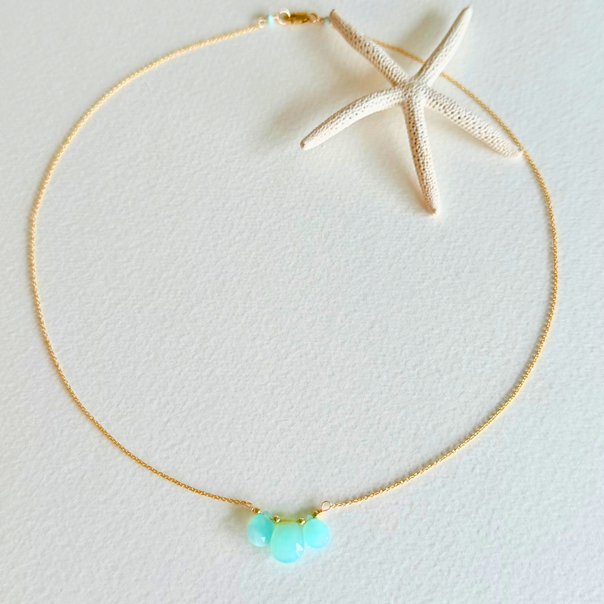 Gold necklace with turquoise beads on a light gray background