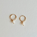 Gold hoop earrings with pearl drops on a light gray background