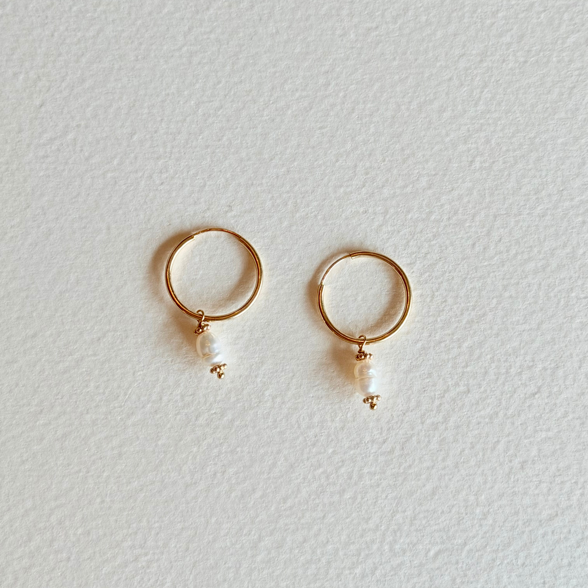 Gold hoop earrings with pearl drops on a light gray background