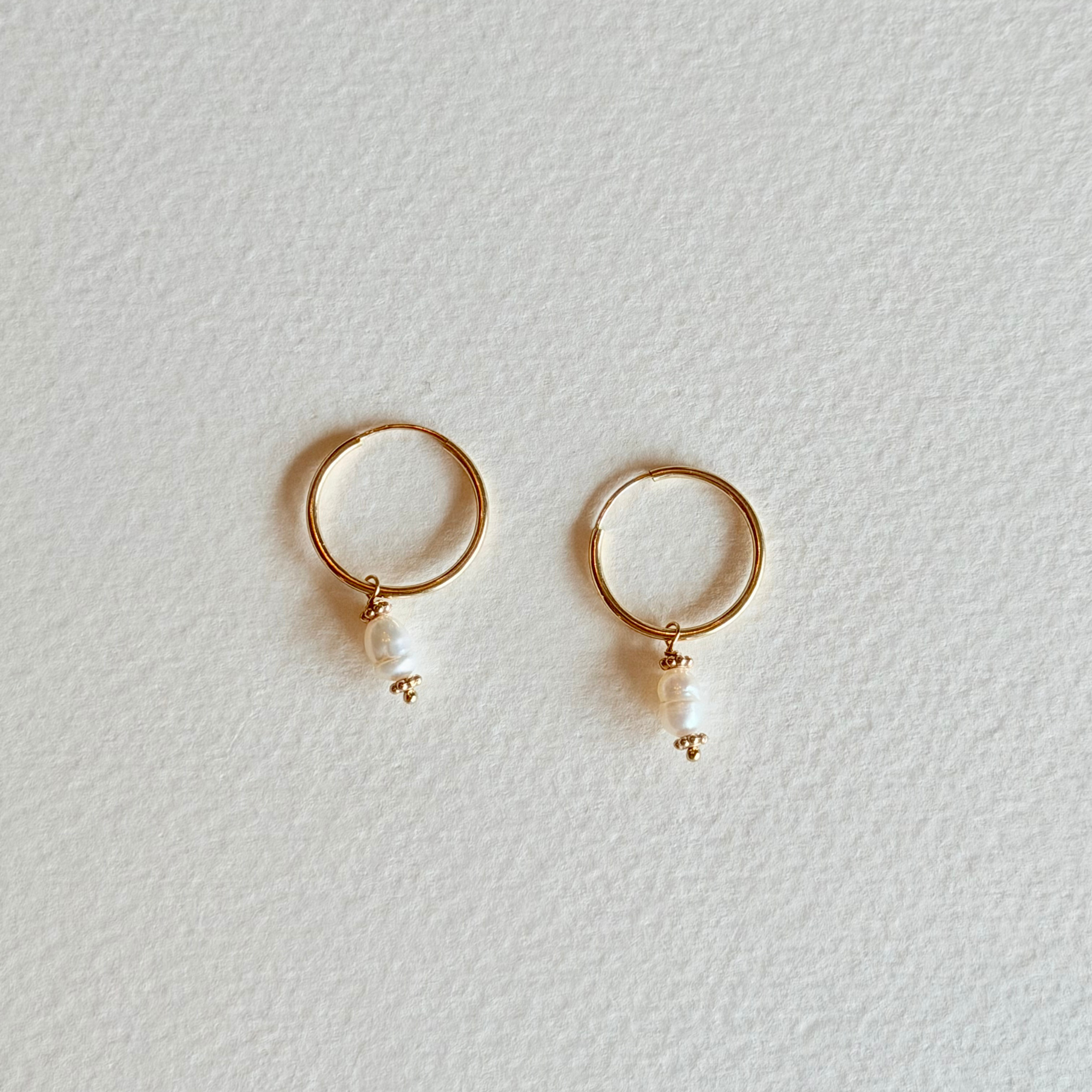 Gold hoop earrings with pearl drops on a light gray background