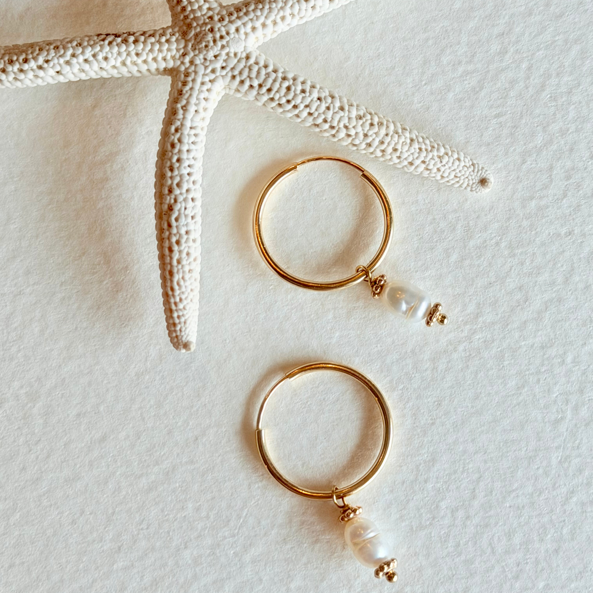 Gold hoop earrings with pearls on a textured white surface with starfish.