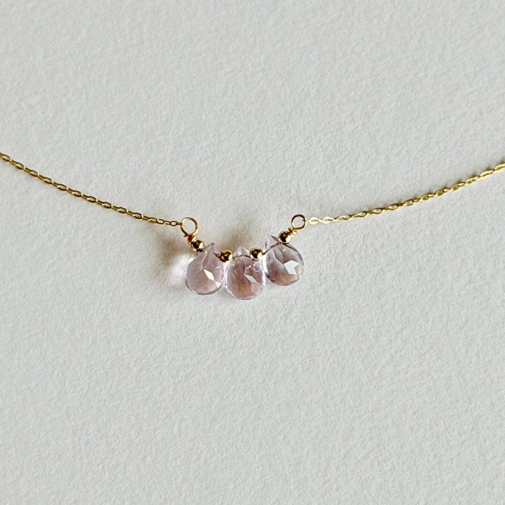Gold necklace with pink beads on a light gray background